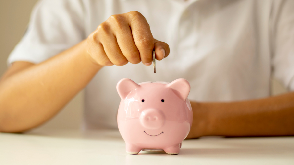 Person Dropping a Coin into a Piggy Bank